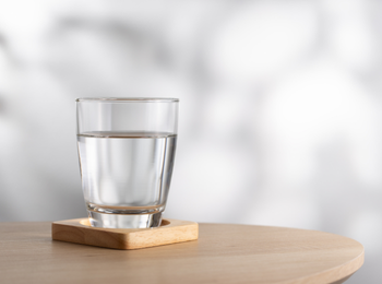 Verre d'eau posé sur un dessous en bois, sur une table claire, illustrant le concept d'investir dans l'eau comme placement durable et essentiel à long terme.
