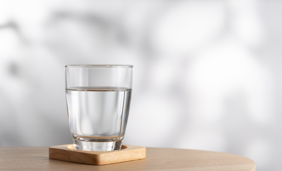 Verre d'eau posé sur un dessous en bois, sur une table claire, illustrant le concept d'investir dans l'eau comme placement durable et essentiel à long terme.