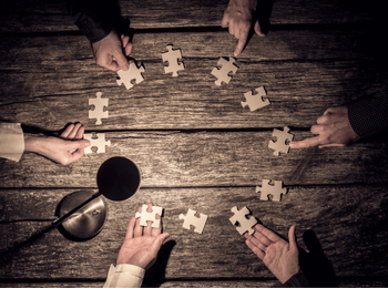 Plusieurs mains assemblant des pièces de puzzle sur une table en bois, symbolisant la déclaration des bénéficiaires effectifs au sein d'une entreprise.