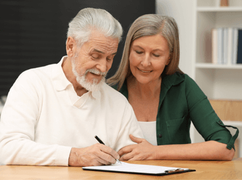 Couple senior souriant en train de signer des documents, illustrant les démarches liées aux frais bancaires en cas de succession.