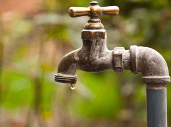 Gros plan sur un robinet ancien avec une goutte d’eau suspendue, illustrant la réforme 2025 sur les redevances de l’agence de l’eau.